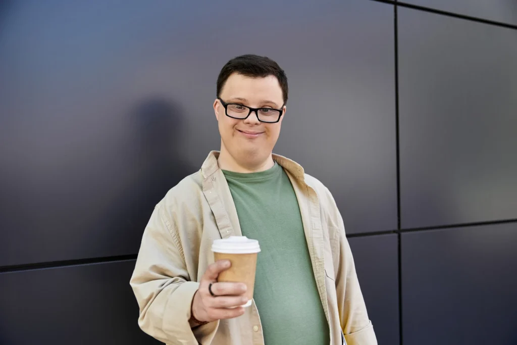 Disabled man with down syndrome holding takeaway coffee and smiling at camera