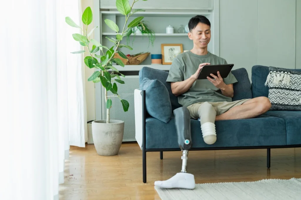Disabled man with amputated leg sitting on couch smiling while looking at iPad